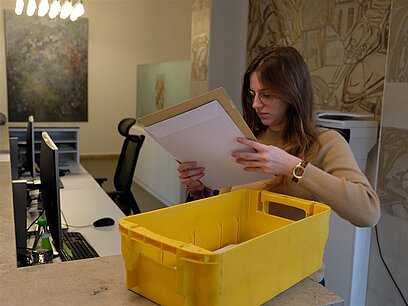 Eine junge Frau nimmt Briefumschläge aus einer gelben Kiste.