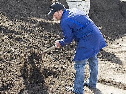 Ein Mann schaufelt in einem Kompostierwerk Erde, um die Verrottung zu prüfen.