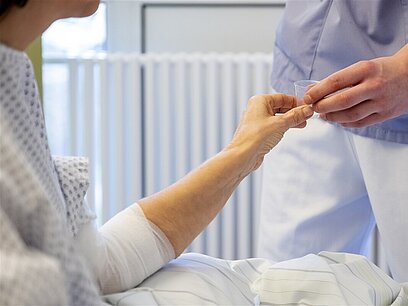 Ein Krankenpflegehelfer versorgt eine Patientin mit Tabletten.
