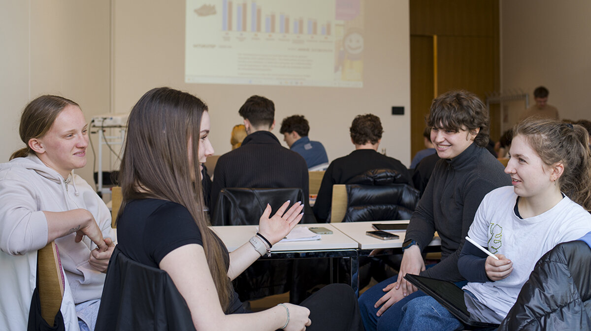 Liselotte sitzt im Klassenzimmer im Wirtschaftslehre-Unterricht und diskutiert in einer Kleingruppe mit Mitschülerinnen und Mitschülern.