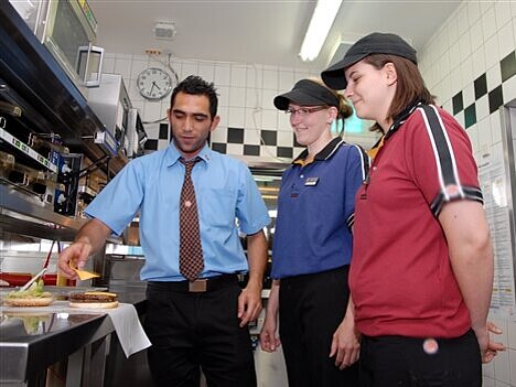 Der Filialleiter zeigt den Fachkräften, wie man einen Burger belegt.