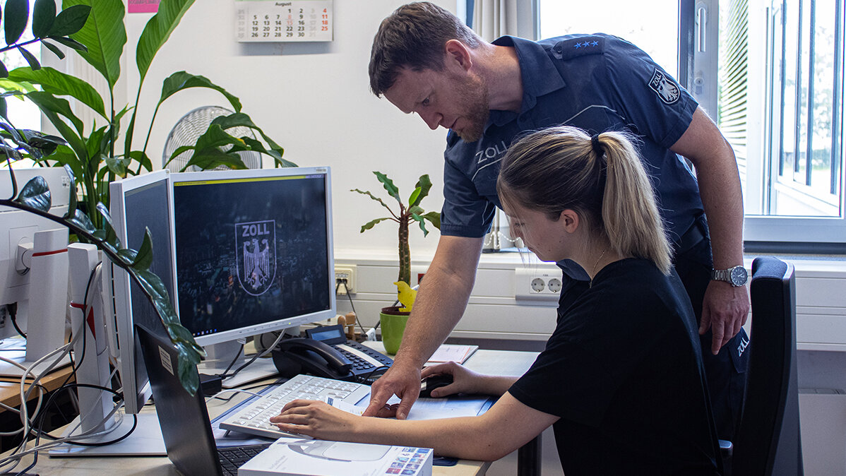 Alicia und ihr Ausbilder bearbeiten die Zollanmeldung am PC im Büro.