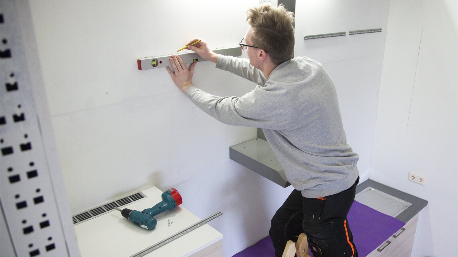 Matthias zeichnet einen Strich an der Wand mit Hilfe der Wasserwaage.