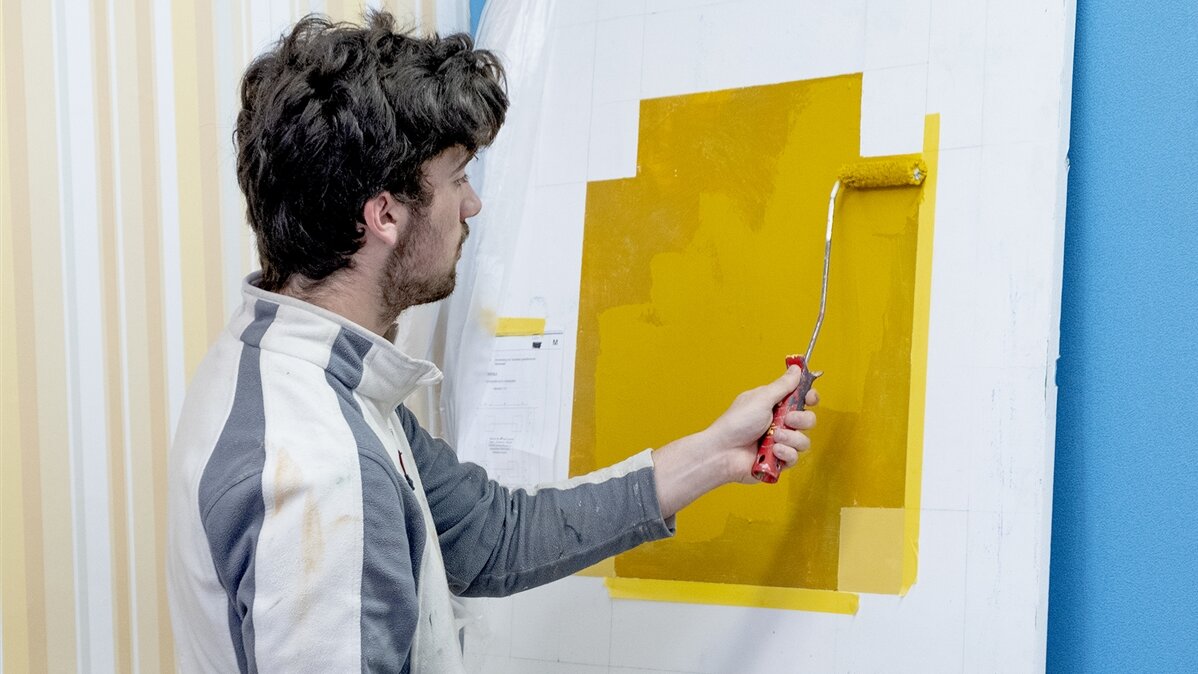 Ein Maler verstreicht gelbe Farbe mit einer Farbwalze.