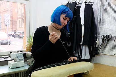 Eine junge Frau näht ein Kleidungsstück mit Nadel und Faden.