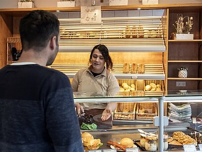Eine junge Frau bedient einen Mann an der Theke in einer Bäckerei.