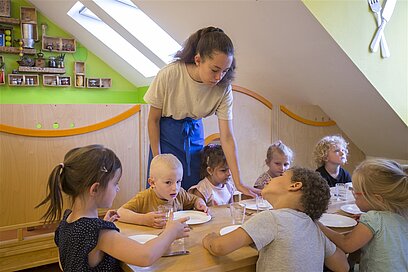 195388 Eine junge Frau stellt kleinen Kindern Geschirr auf den Tisch.