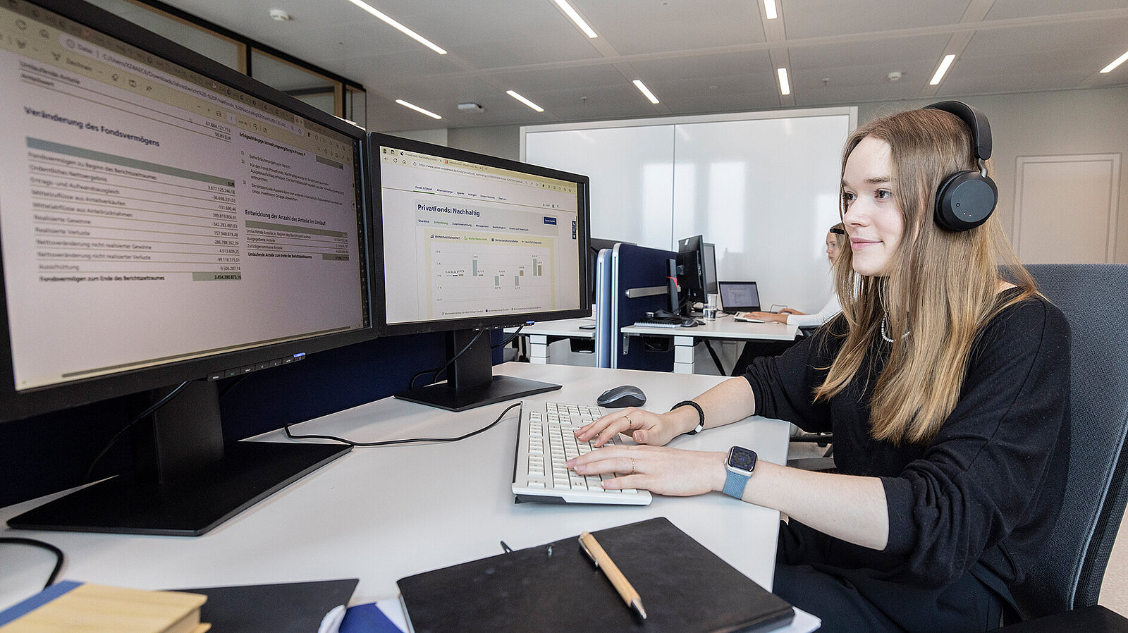 Eine junge Frau arbeitet am Computer und trägt Kopfhörer.