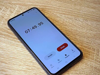 Ein Smartphone mit eingeschalteter Stoppuhr liegt auf einem Untergrund aus Holz.
