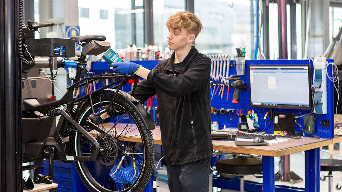 Jakob nimmt in Arbeitshandschuhen in einer Werkhalle Messungen an einem E-Bike vor.