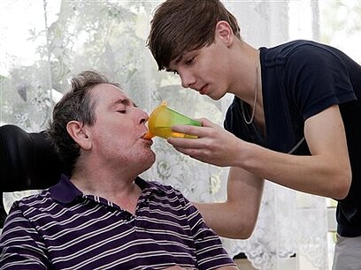 Ein junger Altenpfleger gibt einem älteren Herren Trinken ein.