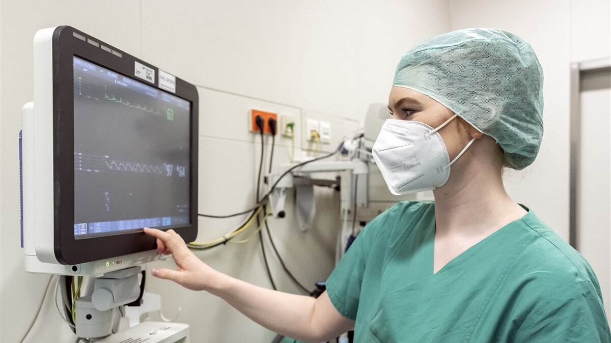 Eine Frau in OP-Kleidung betrachtet die Herzfrequenz auf einem Monitor.