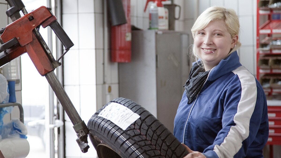Eine junge Frau hält einen Reifen in einer Werkstatt.