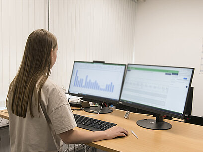 Eine junge Frau blickt auf zwei Computermonitore.