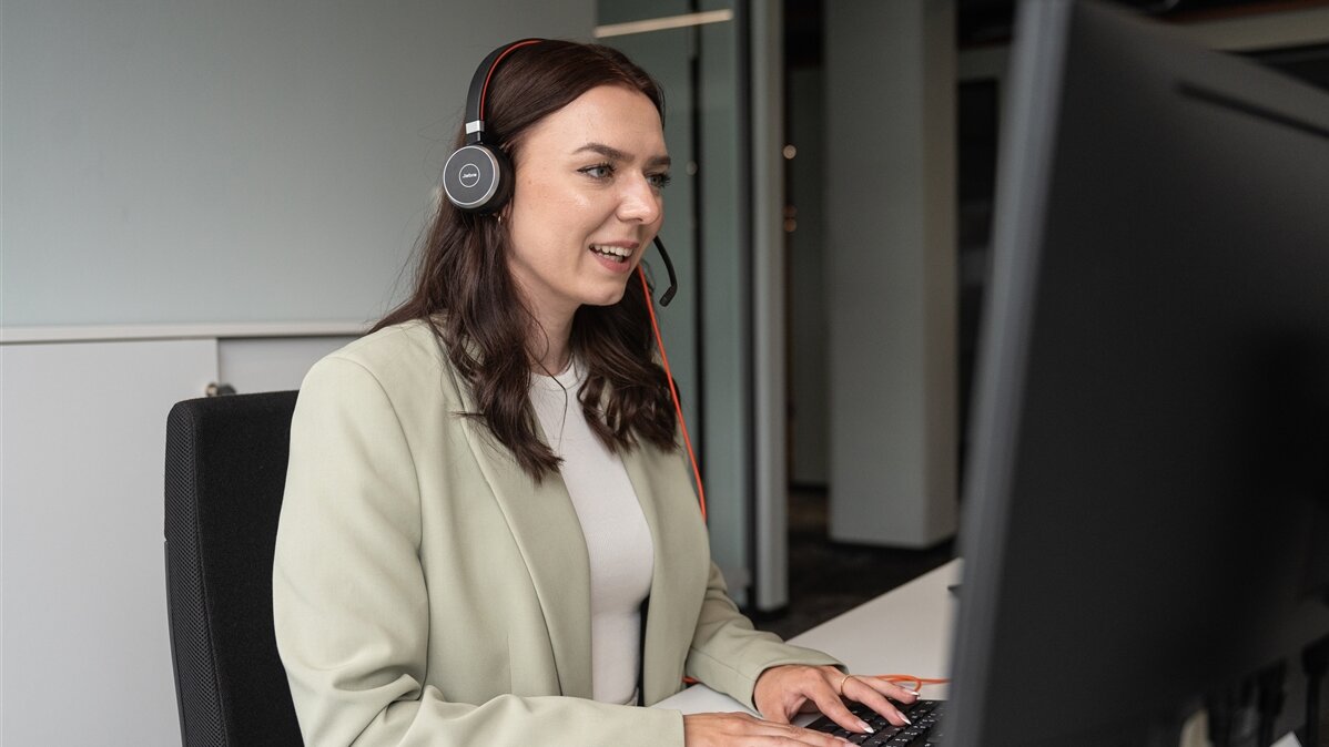 Eine junge Frau mit Headset arbeitet an einem Computer.