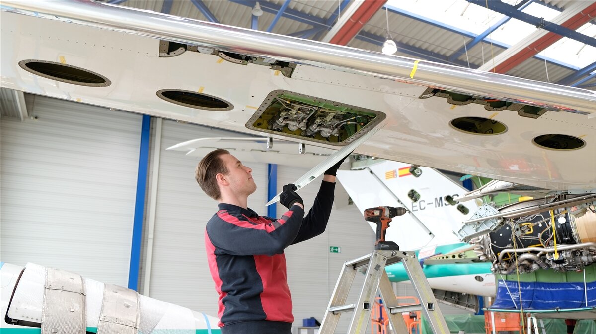 Ein junger Mann entfernt eine Abdeckung an der Tragfläche eines Flugzeug.
