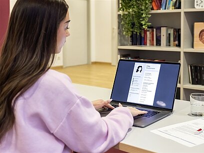 Eine junge Frau sitzt am Schreibtisch und arbeitet an einem Laptop.
