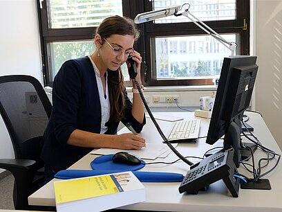 Eine junge Frau telefoniert an ihrem Schreibtisch.