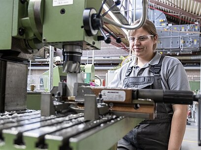 Eine junge Frau mit Schutzbrille steuert eine Maschine.
