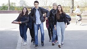 Eine Gruppe von Jugendlichen auf ihrem Weg vor einem Schulgebäude.
