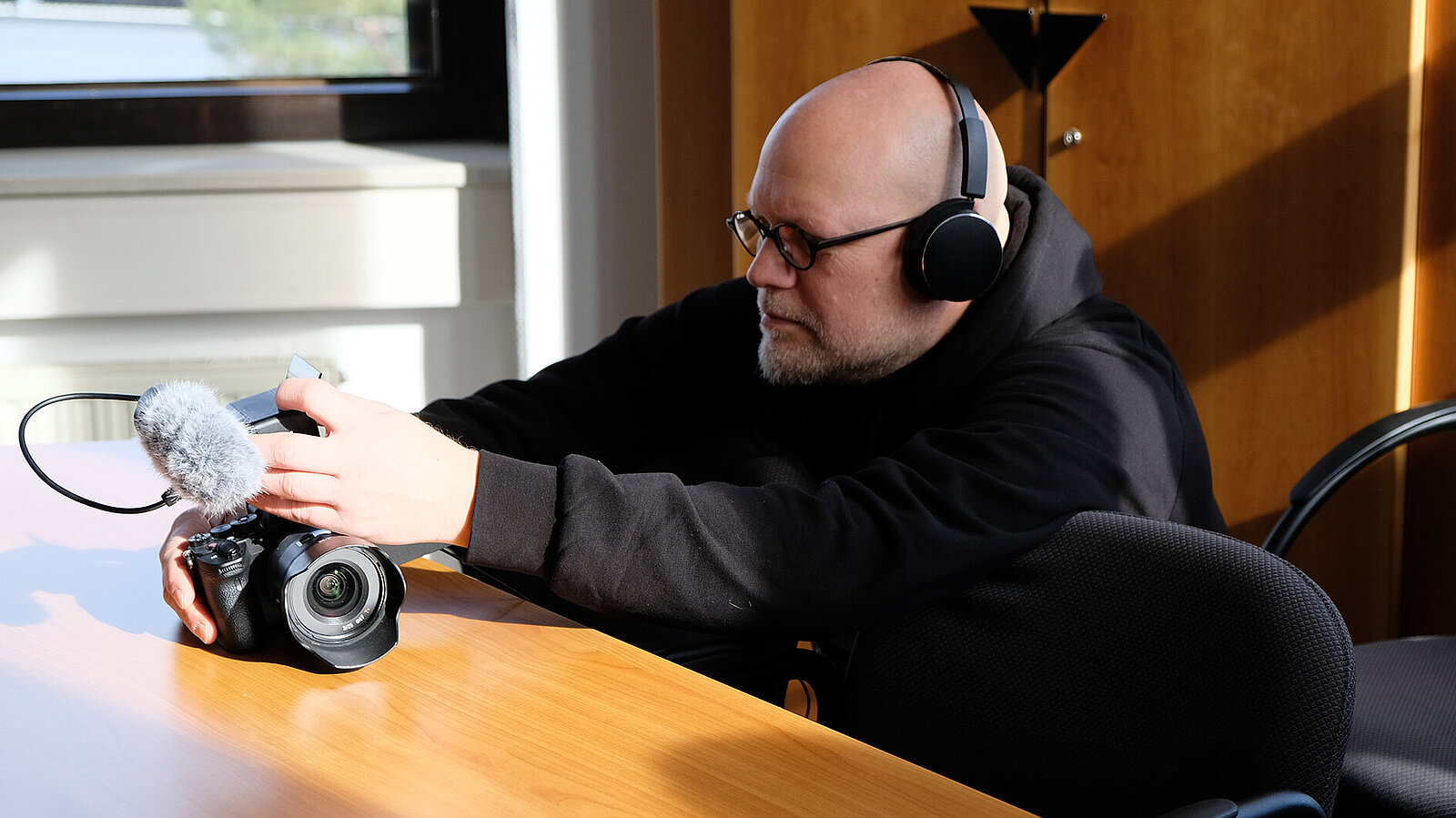 Ein Mann hat Kopfhörer auf und arbeitet mit einer Kamera.