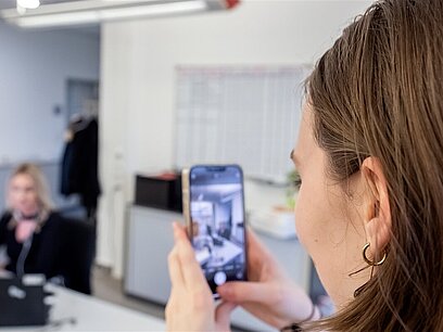 Eine junge Frau macht mit einem Smartphone ein Foto einer anderen Frau im Büro.