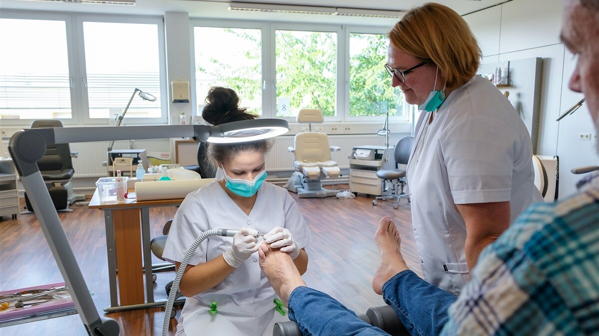 Marie-Louise behandelt den Fuß eines Patienten, während ihre Lehrerin zusieht.