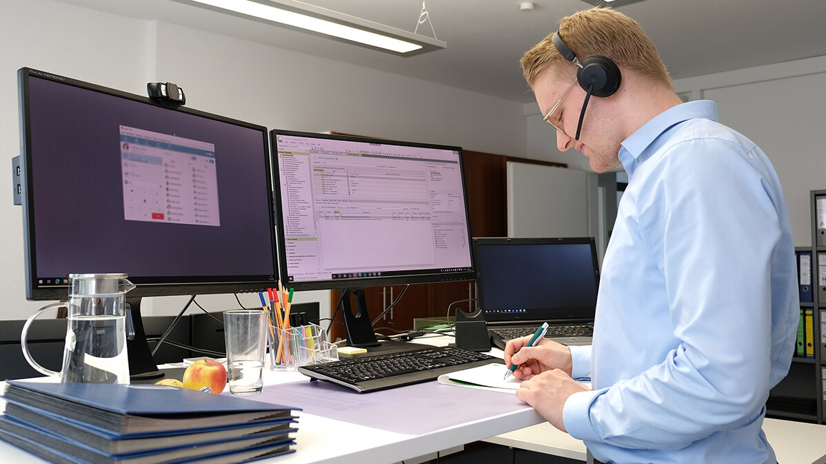 Jonas telefoniert mit Headset und macht sich Notizen.