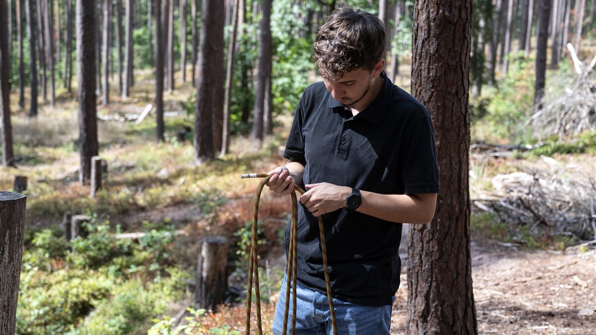 Luis überprüft im Wald ein Seil auf Beschädigungen.