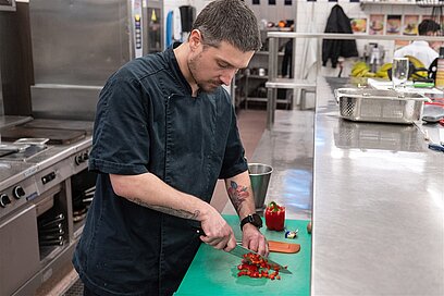 Ein junger Mann steht in einer Restaurantküche und schneidet eine Paprika.