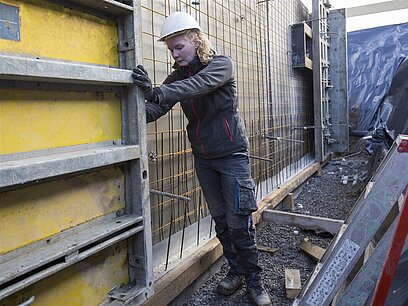 Eine Frau prüft ein Bauteil auf einer Baustelle.