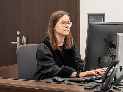 Eine junge Frau trägt eine schwarze Robe im Gericht und tippt konzentriert am Computer.