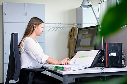Eine junge Frau überprüft abgelegte Daten im Ordner und am Computer.