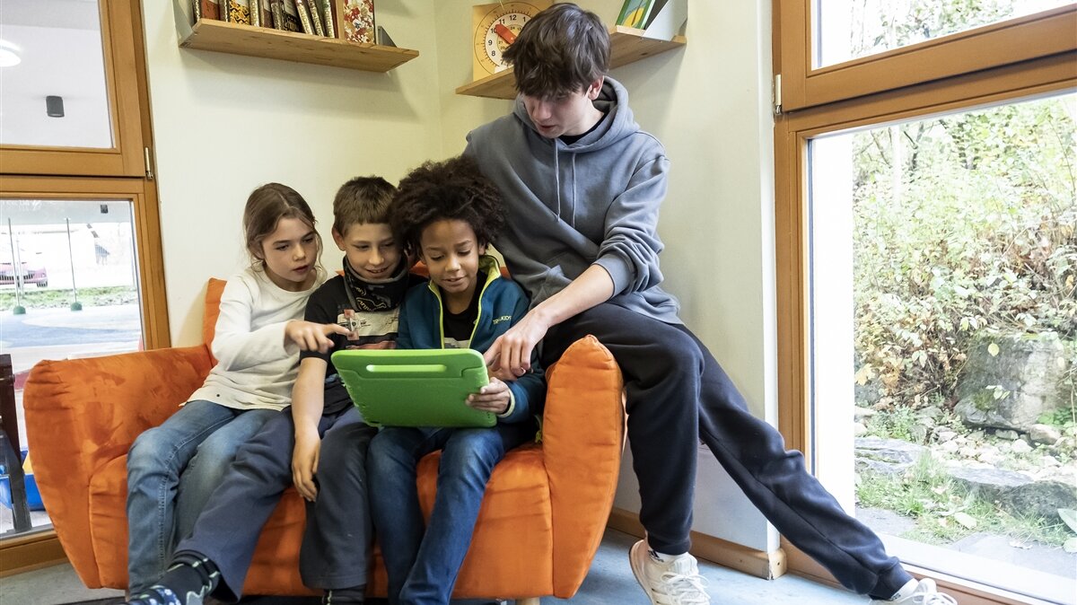 Ein junger Mann zeigt drei Kindern etwas auf einem Lerntablet.