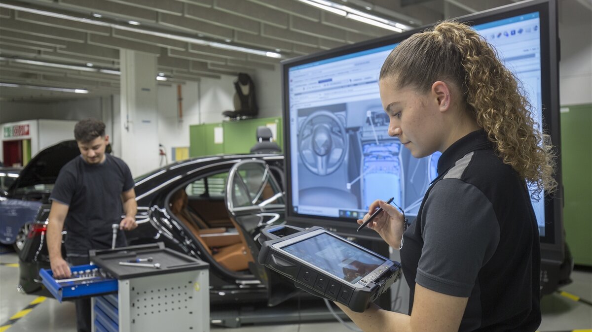 Eine Auszubildende betrachtet auf einem Tablet ein Auto-Bauteil.