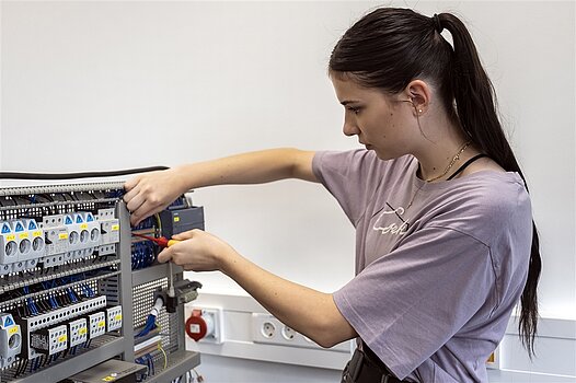 Eine junge Frau arbeitet mit einem Schraubenzieher an einem elektrischen Gerät.