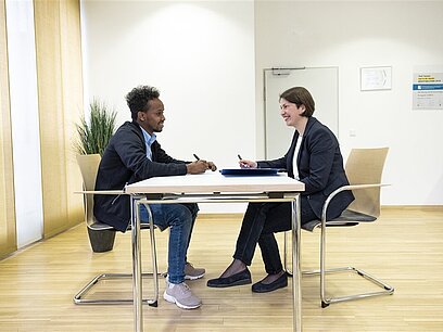 Ein junger Mann und eine Personalerin führen an einem Tisch ein Vorstellungsgespräch.