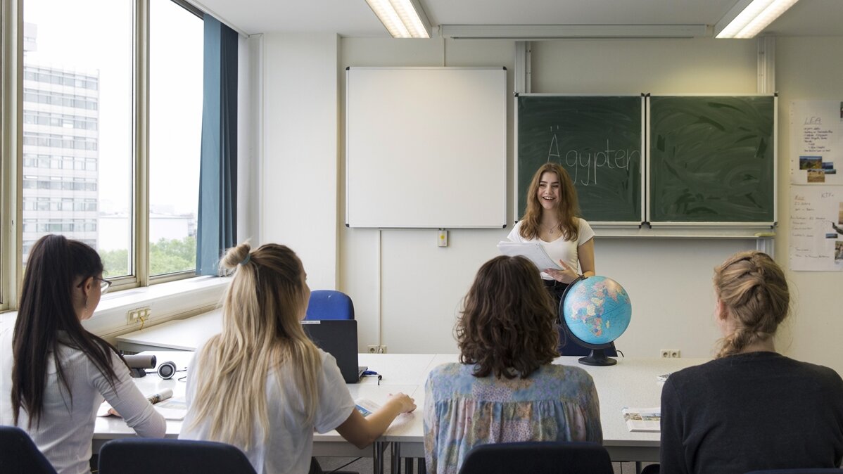 Eine junge Frau steht mit einem Globus vor einer Schulklasse.