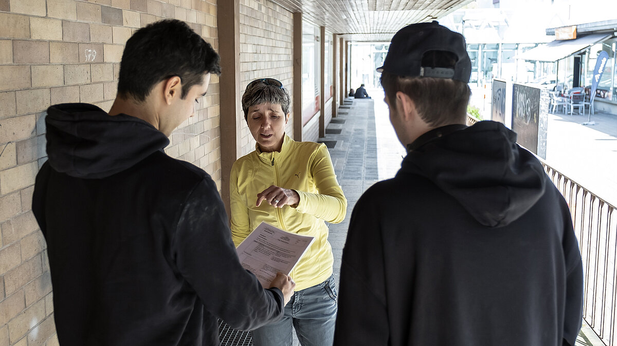 Eine Frau erklärt zwei jungen Männern ein Dokument.