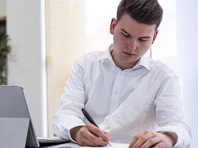 Ein junger Mann schreibt mit einem Kugelschreiber auf ein Papier.