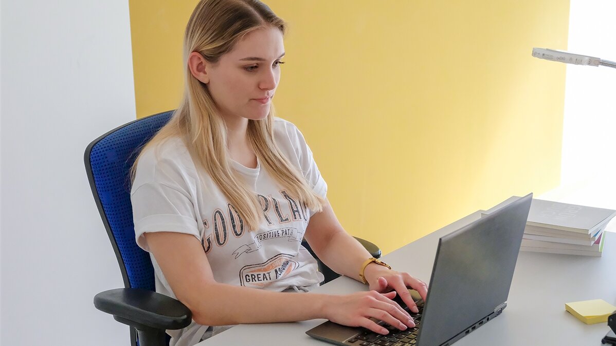 Eine junge Frau tippt etwas in ihren Laptop am Schreibtisch.