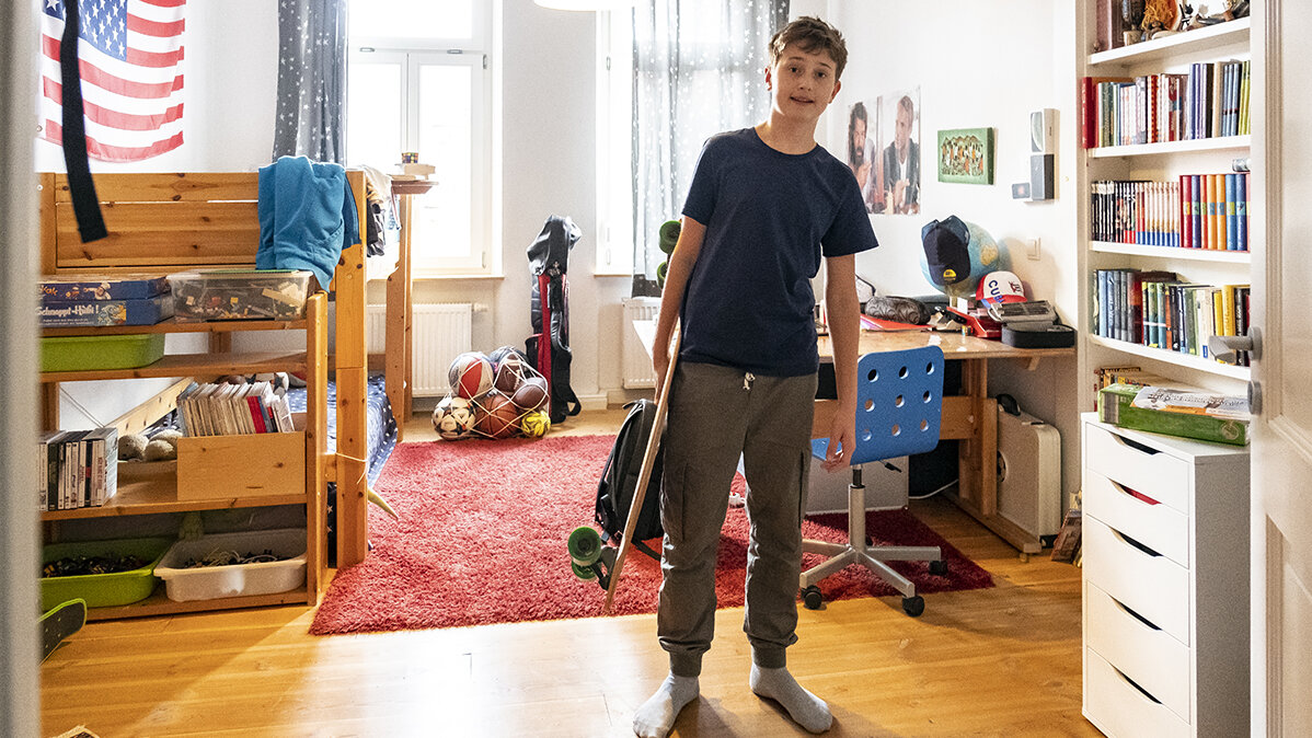 Ein Junge steht mit seinem Skateboard in der Hand in seinem Kinderzimmer.