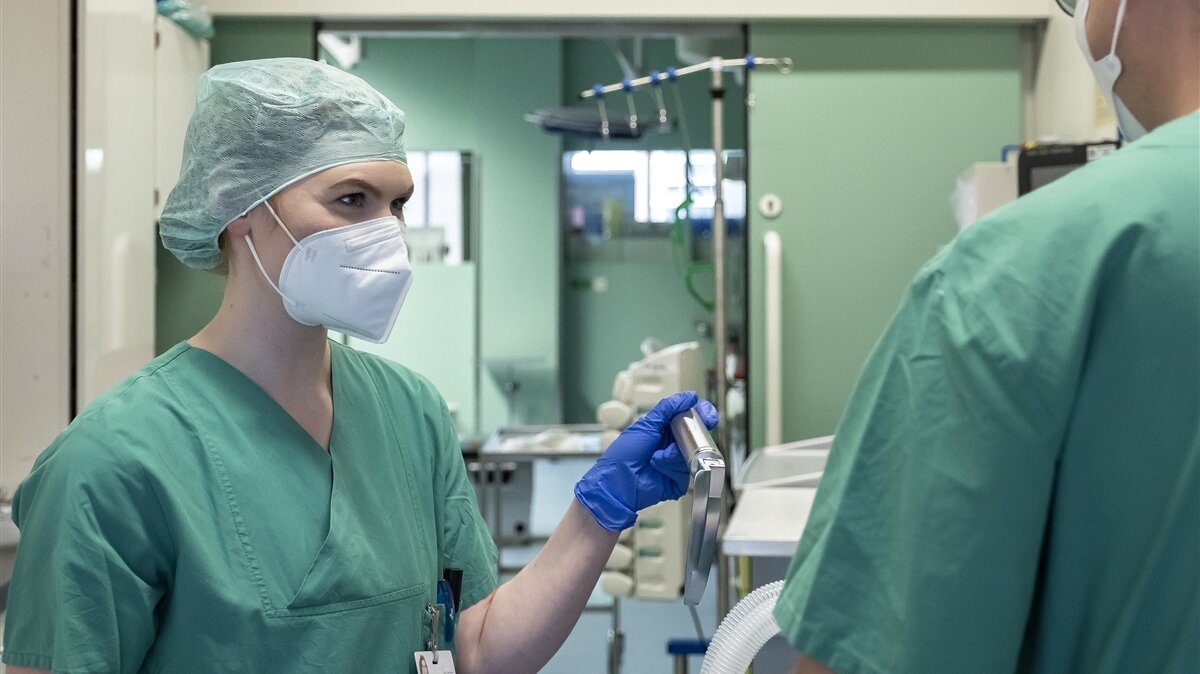 Eine Frau in OP-Kleidung und mit Handschuhen reicht einem Arzt ein medizinisches Gerät.