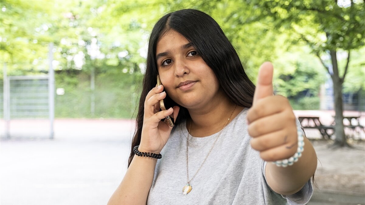 Eine junge Frau gibt einen "Daumen hoch" während sie telefoniert. 