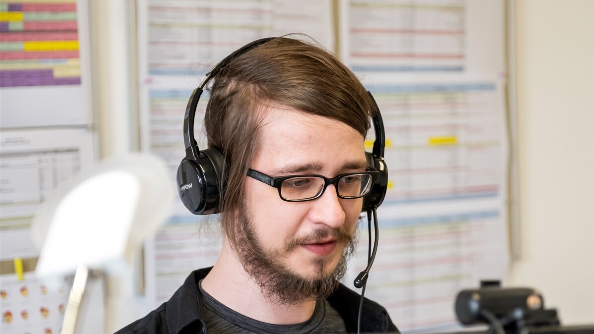 Ein junger Mann mit Headset arbeitet am Bildschirm.