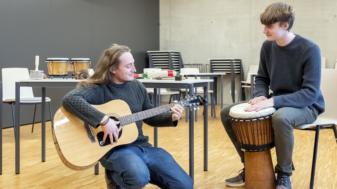 Ein junger Mann spielt Bongo und ein Musiklehrer spielt Gitarre.