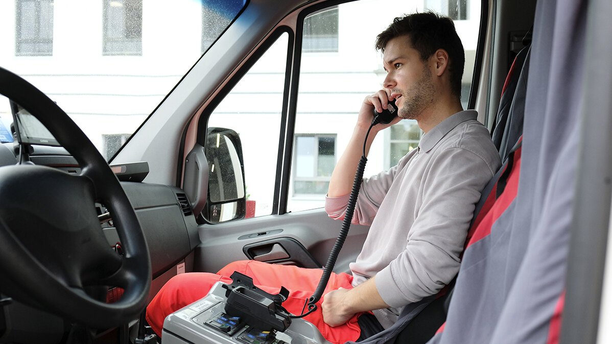 Benjamin sitzt in Arbeitskleidung in einem Rettungswagen und telefoniert.