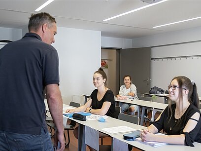 Ein Lehrer steht im Unterrichtsraum vor seiner Klasse.