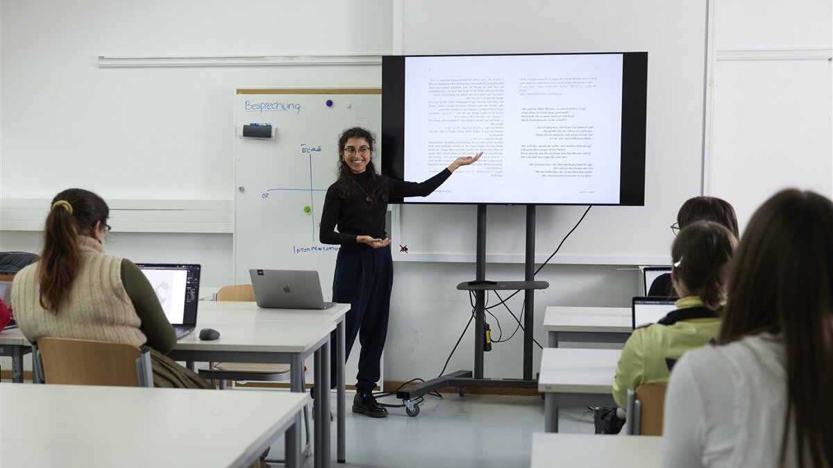 Eine junge Frau hält eine Präsentation vor einer kleinen Gruppe in einem Klassenraum.