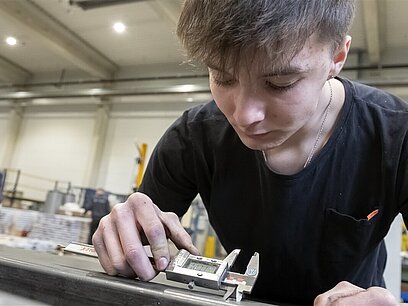 Ein junger Mann prüft mit einem digitalen Messschieber den Durchmesser der Löcher in einem Metallrohr.